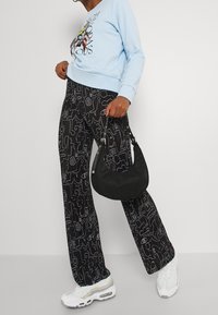 Ljusblå sweatshirt med grafisk tryck, ihop med svarta vida byxor med vita abstrakta linjeteckningar. Svart väska och vita sneakers.