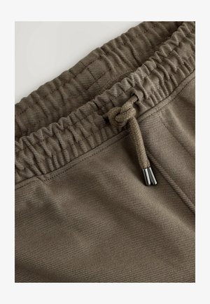 Hnedé textúrované nohavice s elastickým pásom, vybavené šnúrkou s kovovými koncami a zošívacími detailmi pozdĺž okrajov.