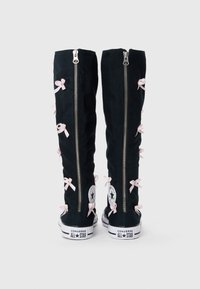 Mustad mustad mustad roosade paelte ja hõbedaste lukkudega. Omab Converse All Star brändingut tallas ja külgpatjadel.