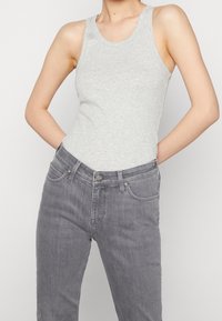 Lichtgrijze tanktop van een zachte stof met een ronde halslijn, gecombineerd met donkergrijze jeans met een middelhoog model, zijzakken en een knoopsluiting.