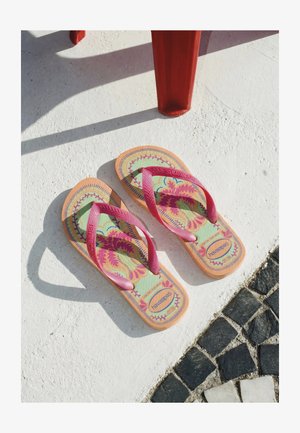 Bunte Flip-Flops mit pinkfarbenen Riemen auf weißem strukturiertem Boden nahe einem roten Stuhlbein und schwarz-weißen Mosaikfliesen.