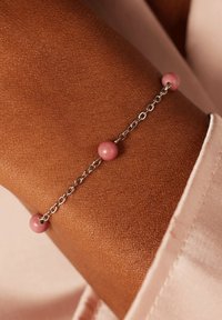 Zilveren kettingarmband met drie roze ronde kralen. De kralen zijn glad en glanzend, in contrast met de textuur van de huid eronder.
