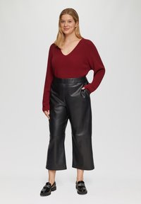 Bordeaux gebreide trui met V-hals, gecombineerd met hoge zwarte leren culottes. Model draagt zwarte instappers. Eenvoudig, modern ontwerp.