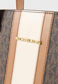 Pruunide ja beežide nahkkäekott logoga kuldsel riistvaral, beeži ja pruuni triibulise mustriga. Tekstuuriga taustadetail.