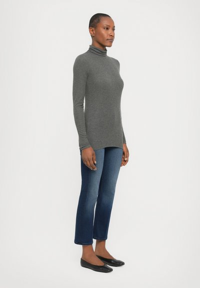 Grå turtleneck langermet topp, slim fit, kombinert med mørkeblå jeans, cropped stil, og svarte ballerinasko på en ensfarget bakgrunn.