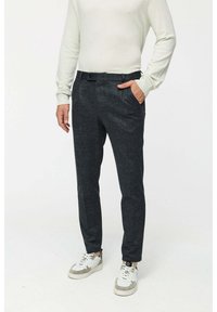 Dunkelgraue, strukturierte Hose mit einer taillierten Passform, ausgestattet mit seitlichen Taschen und flachem Bund. Getragen mit einem weißen Langarmoberteil und Turnschuhen.