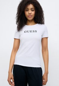 White short-sleeve t-shirt made of soft fabric, featuring a round neckline and the word "GUESS" in bold black letters across the chest.