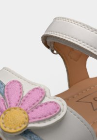 Λευκό παπούτσι με φαρδιά ταινία, που διαθέτει σχέδιο με ροζ μαργαρίτα με κίτρινο κέντρο. Απαλό γαλάζιο διακοσμητικό ρίγισμα στο πλάι.