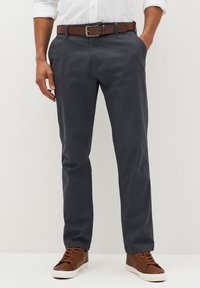 Chinos grigi scuri realizzati in tessuto testurizzato, dotati di tasche laterali e indossati con una cintura marrone e sneakers in pelle marrone.