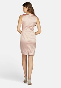 Robe en satin rose sans manches avec une silhouette ajustée, fermeture éclair au dos et deux poches latérales. Longueur au genou avec une petite fente au dos.