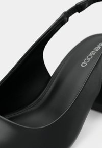 Gros plan d'une chaussure à talon haut slingback en cuir noir avec un talon bloc et une semelle intérieure cousue.