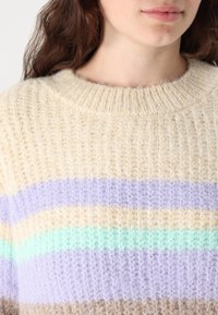 Megztinis su raukšlėtu apvaliu kaklu, pagamintas iš kreminės, levandų, mėtų žalios ir šviesiai rudos juostų mišinio. Minkšta tekstūra.