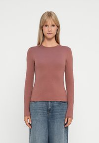 T-shirt à manches longues, ajusté, en rose poussiéreux, fabriqué en coton lisse. Encolure ronde, coutures minimales, associé à un jean large bleu clair.