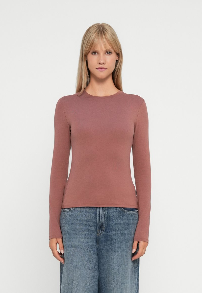 T-shirt à manches longues, ajusté, en rose poussiéreux, fabriqué en coton lisse. Encolure ronde, coutures minimales, associé à un jean large bleu clair.
