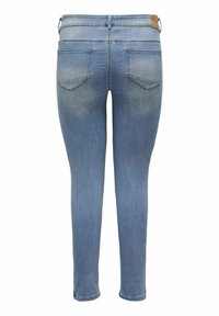 Chudé džínsy vo svetlom modrom denime so slabým vyblednutím. Obsahujú dve zadné vrecká a hnedú koženú nášivku na pasaž. 