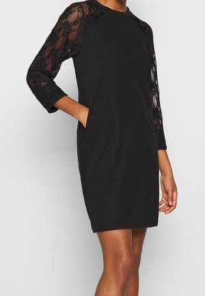 Zwarte jurk met driekwart kanten mouwen, afgeronde halslijn, losse pasvorm, zijzakken en textuurdetails van kant op de mouwen.
