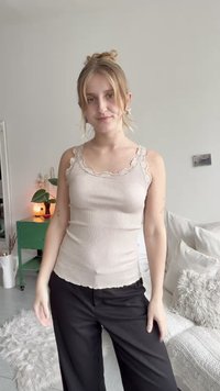 Light beige ribbed tank top with lace trim, fitted design and scalloped hem, paired with black wide-leg pants.