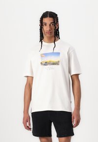 Hvid bomulds t-shirt med et farverigt grafisk print af en vintage bilscene, med korte ærmer og en afslappet pasform. Sorte shorts.