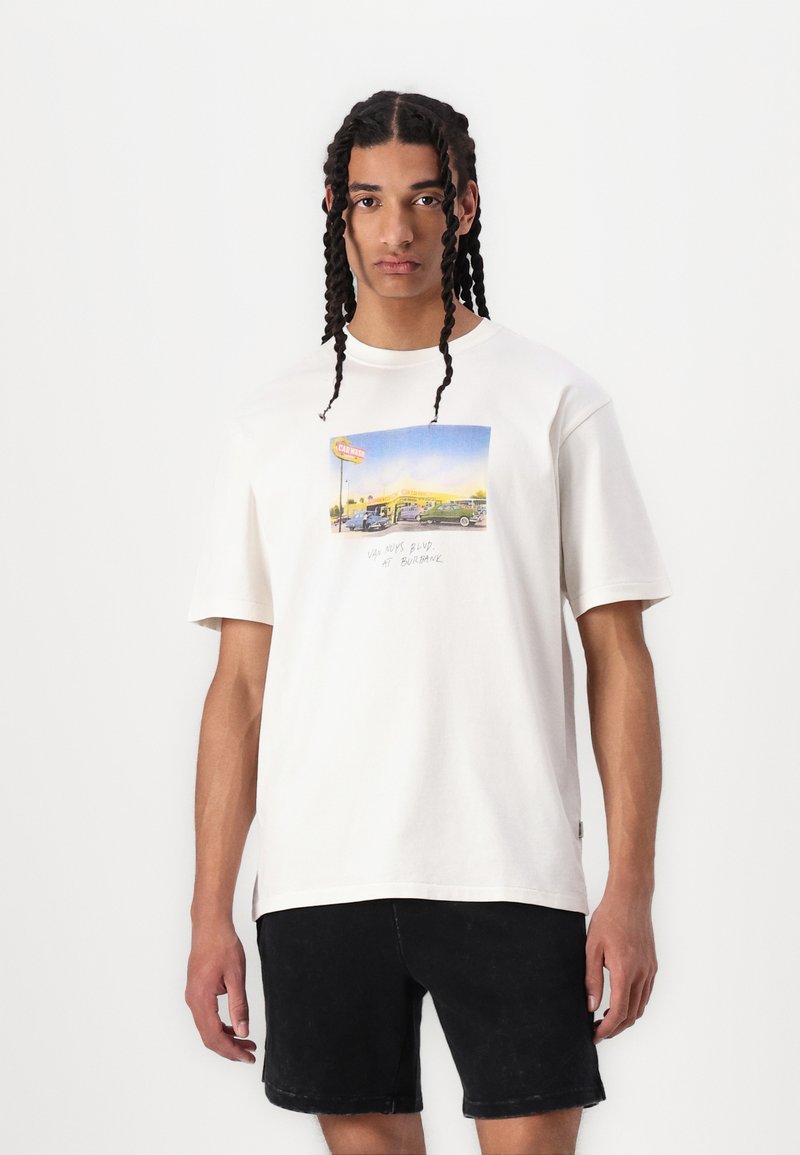 Hvid bomulds t-shirt med et farverigt grafisk print af en vintage bilscene, med korte ærmer og en afslappet pasform. Sorte shorts.