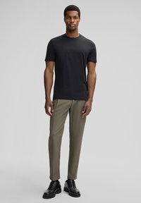 Zwarte T-shirt met korte mouwen, gecombineerd met olijfgroene broek en zwarte veterschoenen. De outfit heeft een ronde hals en een getailleerd silhouet.