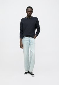 T-shirt à manches longues côtelé bleu marine, jean bleu clair coupe décontractée, baskets noires avec semelles blanches, mannequin debout devant un fond uni.