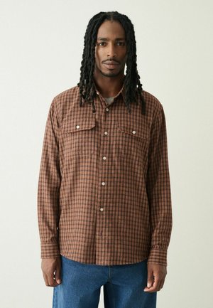 Braun karierte langärmlige Hemd mit zwei Brusttaschen, Knopfverschluss und lässiger Passform; getragen mit hellblauen Jeans.