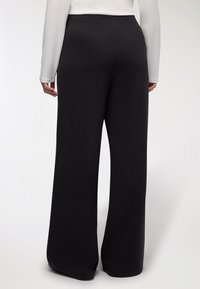 Pantaloni neri a gamba larga realizzati in stoffa morbida, con una vita elastica e una superficie liscia e uniforme senza motivi.