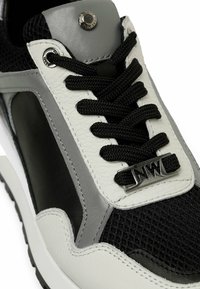 Le sneakers bianco e nere presentano un tessuto a rete, dettagli in pelle, pannelli grigi a contrasto, lacci strutturati e un logo metallico laterale.