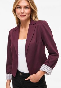 Blazer bordeaux au design ajusté, avec un revers cranté et des poignets rayés. Confectionné dans un tissu lisse, coupe moderne et accents contrastants.
