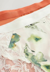 Monivärinen kukkakuvioinen kangas, jossa vihreitä ja keltaisia yksityiskohtia, yhdistettynä oranssiin osioon ja valkoiseen pitsireunaan reunoilla.