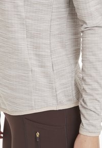 Ljusgrå randig långärmad skjorta med en figurnära design, som har en krämfärgad fåll och sömdetaljer, i kombination med mörkbruna leggings.