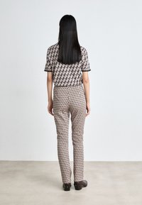 Bedruckte Bluse und enganliegende Hose mit geometrischem Muster in sanften Farben. Glattes Gewebe mit schwarzem Besatz und einem eleganten, maßgeschneiderten Design.