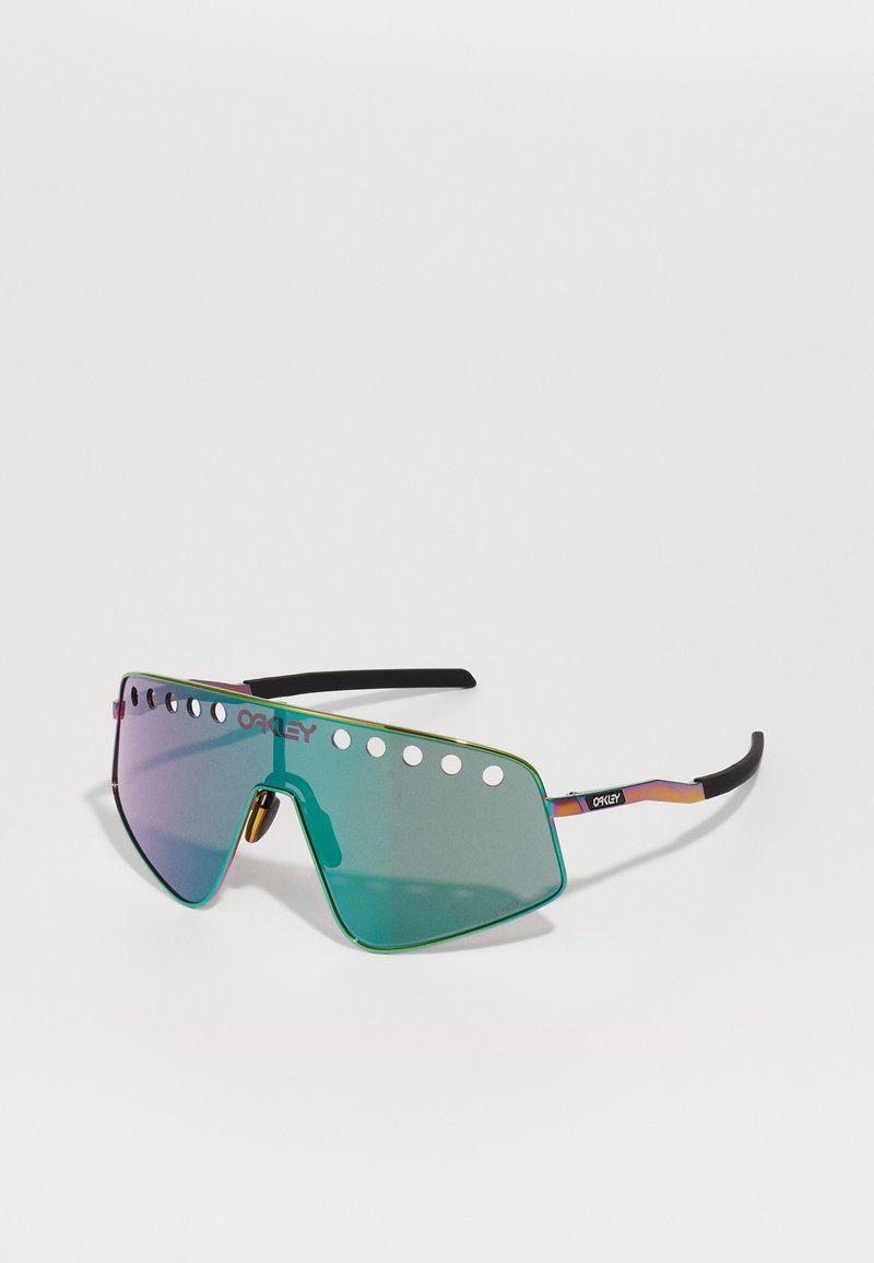 Ochelarii de soare Oakley au un lentilă mare, cu oglindă verde, cu decupaje în partea de sus, un design elegant unghiular și un cadru metalic colorat cu vârfuri negre.