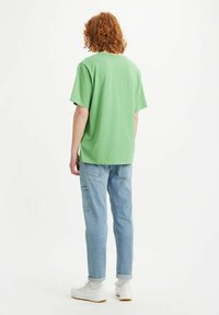 Zelené bavlněné tričko s krátkým rukávem, kulatým výstřihem a volným střihem. V kombinaci se světle modrými džínovými kalhotami s užitečnými kapsami. Viditelné bílé tenisky.