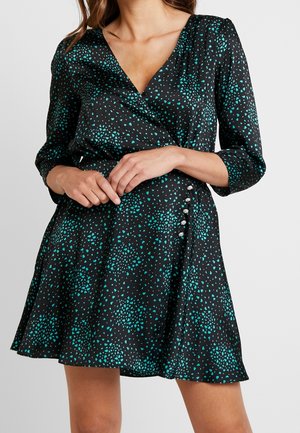 Robe portefeuille noire avec un motif de points dispersés teal, manches trois-quarts, et boutons décoratifs argentés sur le côté de la taille.