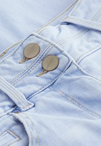 Pantalons en denim bleu clair avec deux boutons ronds en bronze, des coutures visibles et une texture lisse, mettant l'accent sur la zone de la taille.