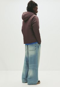 Vadderad huva-jacka i mörklila med en åtsittande midja. Löst sittande ljusblå jeans med ett blekt mönster, i kombination med mörka skor.