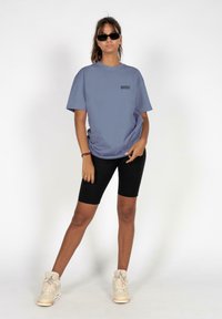 Lys blå oversized t-shirt med korte ærmer, sorte cykelsorte og cremefarvede høj-top sneakers. Model iført mørke solbriller.