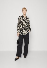 Langermet bluse med et svart og beige abstrakt mønster, parret med svarte cargo-bukser og svarte flate sko.