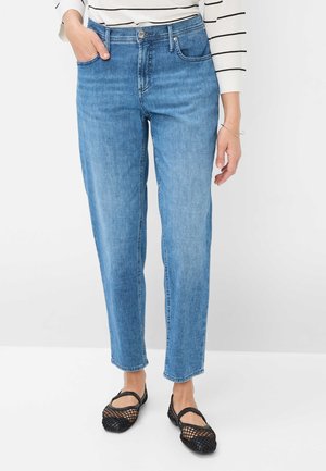 Hellblaue Straight-Leg-Jeans mit einer subtilen Waschung, Gürtelschlaufen und Fronttaschen. Kombiniert mit schwarzen Mesh-Schlupfschuhen.