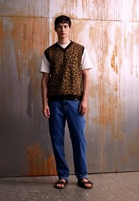 Gilet a stampa leopardata marrone sopra una camicia bianca, abbinato a jeans blue e sandali marroni. Texture morbide e vestibilità casual. Sfondo neutro.