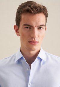 Jasnoniebieska koszula zapinana na guziki o gładkiej fakturze, klasycznym kołnierzyku i białych guzikach. Charakteryzuje się dopasowanym krojem i gładkim wyglądem.