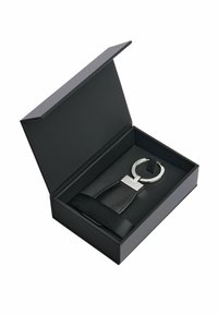 Czarny skórzany brelok do kluczy z okrągłym metalowym pierścieniem, zaprezentowany w czarnym pudełku z zamknięciem na wstążkę. Posiada elegancki design i gładką fakturę.