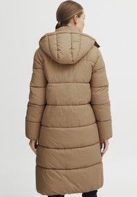 Brun puffig jacka med huva, med ett quiltat mönster och knä-lång passform. Tillverkad av ett smidigt, lätt material.