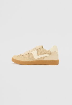 Beige tossud ja võrgumaterjalidega sneaker, ümmargune kuju, silmatorkav pehmendatud krae ja kummist põhi. Omab lainekujulist disaini aksenti.