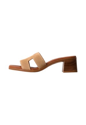 Sandalia mule de ante beige con puntera abierta, tacón bloque de madera y una tira ancha que presenta un recorte rectangular.