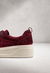 Baskets bordeaux avec un motif texturé en forme de filet et une semelle blanche épaisse sur une surface et un fond gris clair.