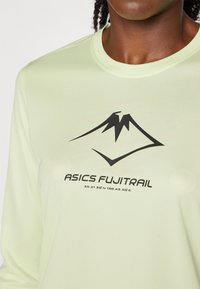 Vihreä pitkähihaisen paita, joka on valmistettu kosteutta siirtävästä kankaasta. Paidassa on musta vuoristologomerkki ja teksti "ASICS FUJITRAIL" keskellä.