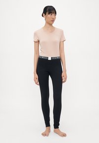 Ljusrosa kortärmad topp med rund halsringning, matchad med svarta leggings som har en kontrasterande märkescinching. Modell som står barfota.