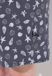 Tessuto grigio con motivi bianchi di conchiglie marine e stelle marine. Include un piccolo etichetta nera sulla cucitura laterale. Materiale morbido e leggero.